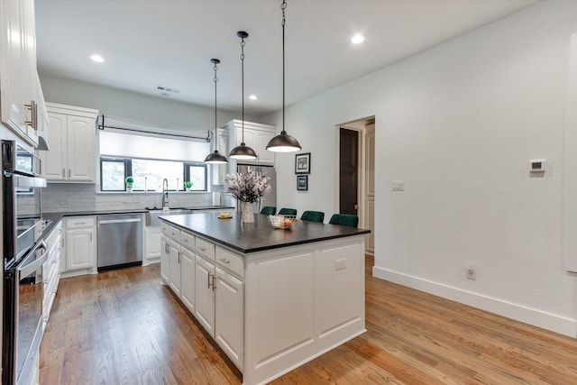 kitchen with white cabinetry, tasteful backsplash, a kitchen island, appliances with stainless steel finishes, and light hardwood / wood-style flooring