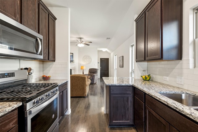 kitchen featuring appliances with stainless steel finishes, backsplash, light stone counters, dark brown cabinetry, and dark wood-type flooring