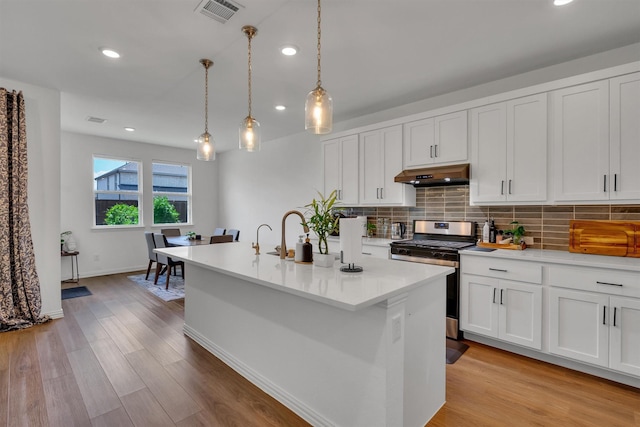 kitchen featuring stainless steel gas stove, an island with sink, pendant lighting, white cabinets, and tasteful backsplash