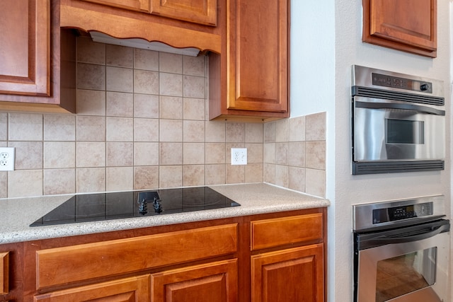 kitchen featuring black electric stovetop, light stone countertops, decorative backsplash, and double oven