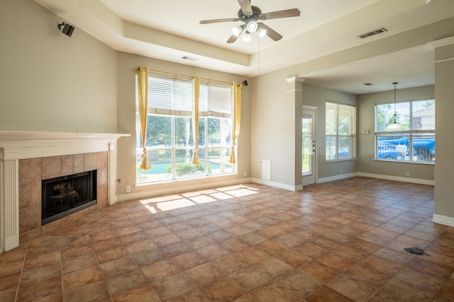 unfurnished living room with a tray ceiling, a tile fireplace, dark tile patterned flooring, and ceiling fan