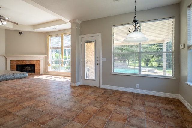 interior space featuring dark tile patterned floors, a tray ceiling, a tiled fireplace, and ceiling fan