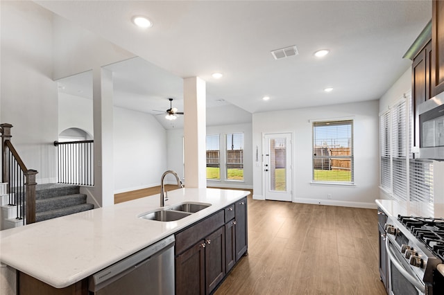 kitchen with stainless steel appliances, dark brown cabinetry, sink, a kitchen island with sink, and light hardwood / wood-style flooring