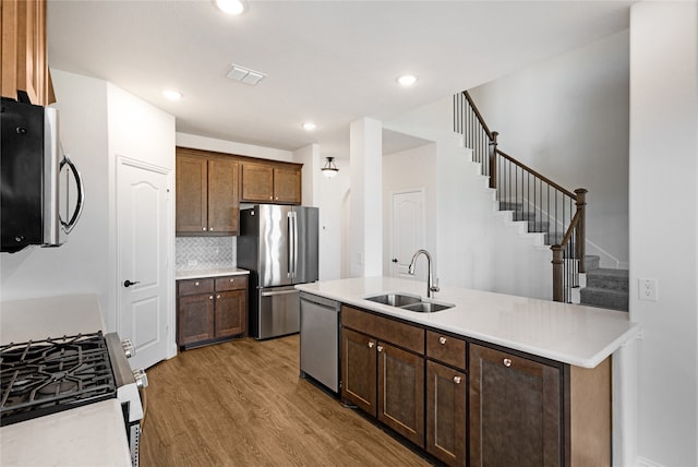 kitchen featuring sink, appliances with stainless steel finishes, tasteful backsplash, wood-type flooring, and a kitchen island with sink