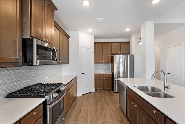 kitchen with light hardwood / wood-style floors, stainless steel appliances, light stone counters, sink, and tasteful backsplash