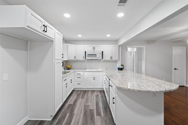 kitchen featuring visible vents, a peninsula, white microwave, and white cabinetry