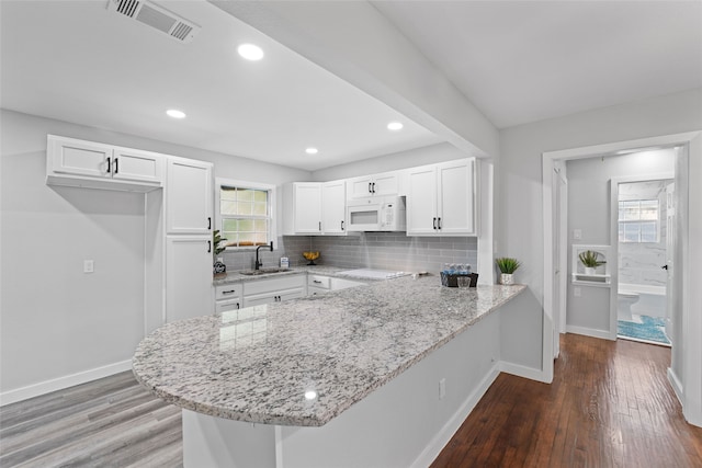 kitchen with light stone countertops, white cabinets, wood-type flooring, and plenty of natural light