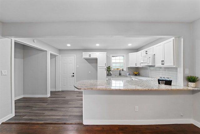 kitchen with white microwave, dark wood-type flooring, white cabinets, light stone countertops, and a peninsula