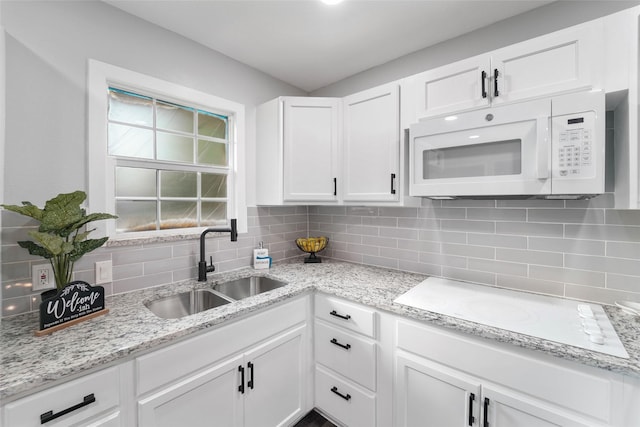 kitchen featuring tasteful backsplash, white cabinetry, a sink, and white microwave