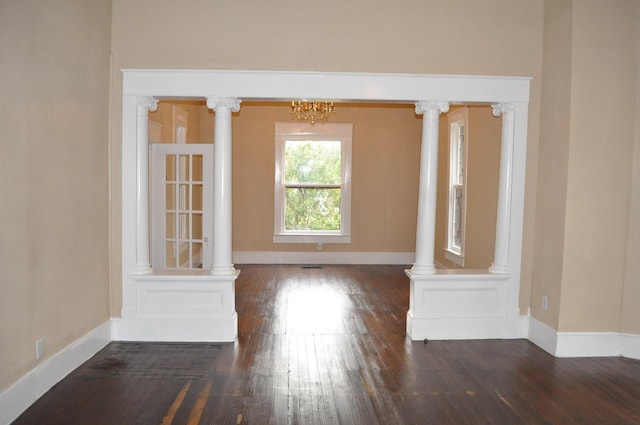 empty room with ornate columns, dark wood-type flooring, and an inviting chandelier