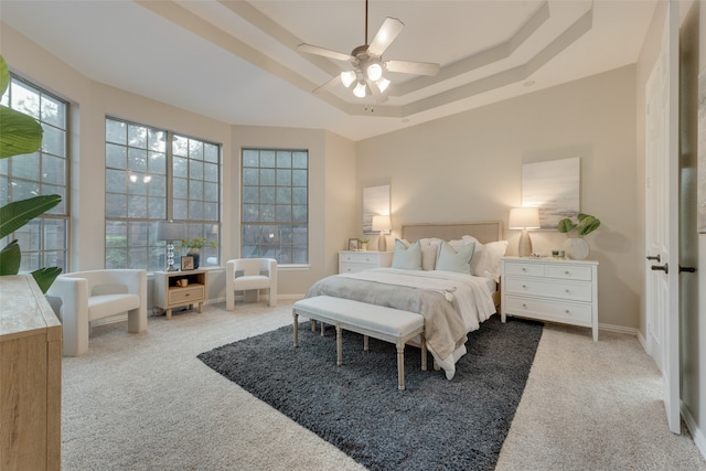 carpeted bedroom with ceiling fan, multiple windows, and a tray ceiling