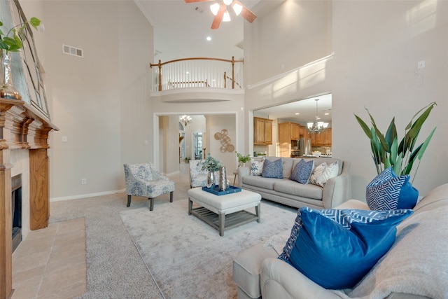 carpeted living room with ceiling fan with notable chandelier, a towering ceiling, and a fireplace