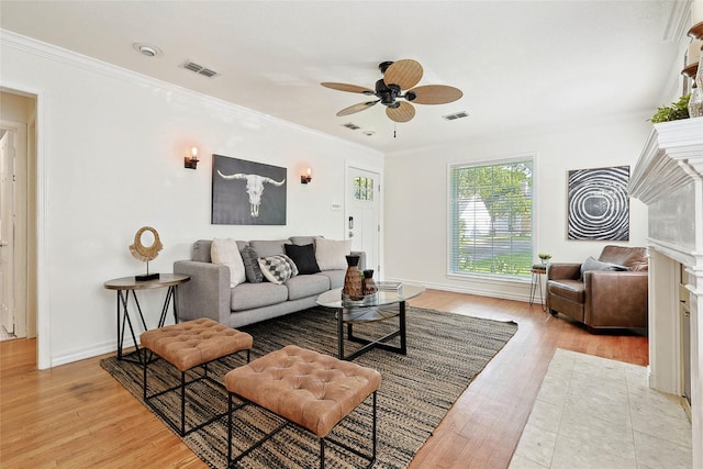 living room featuring ceiling fan, crown molding, light wood-type flooring, and a fireplace