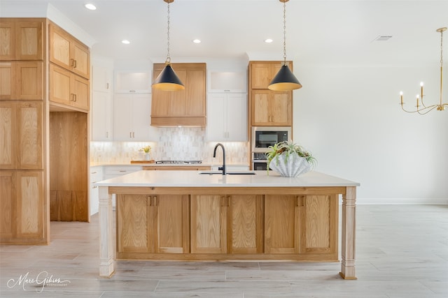 kitchen with black microwave, hanging light fixtures, sink, decorative backsplash, and a center island with sink