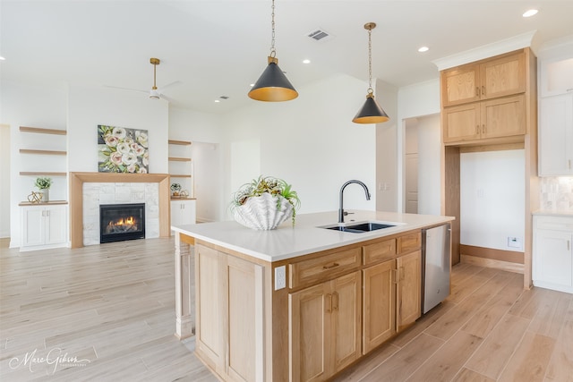 kitchen featuring a stone fireplace, light hardwood / wood-style floors, a kitchen island with sink, and stainless steel dishwasher