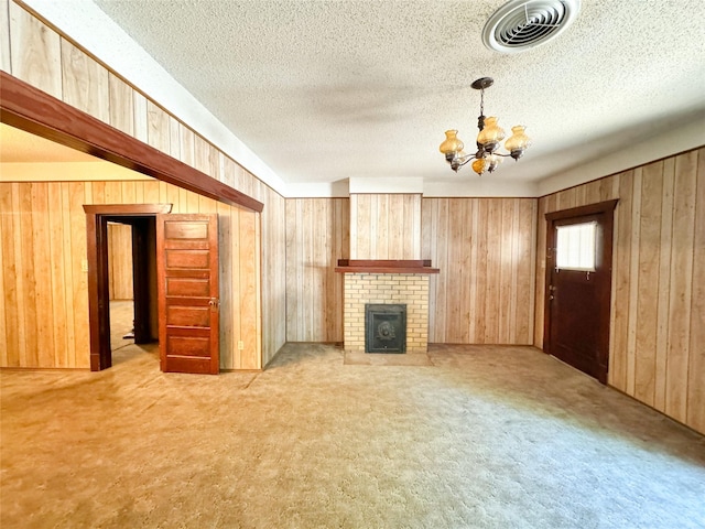 unfurnished living room featuring a notable chandelier, a textured ceiling, a brick fireplace, wooden walls, and light colored carpet