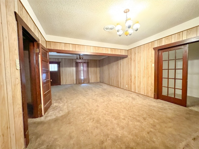 spare room with a textured ceiling, carpet, a notable chandelier, and wooden walls