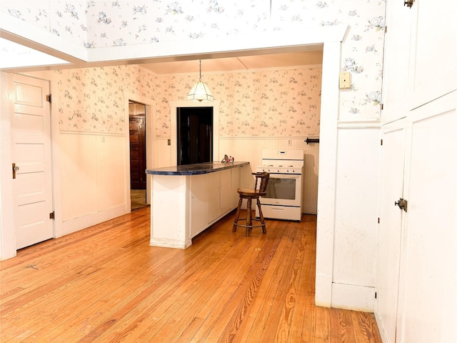 kitchen with kitchen peninsula, hanging light fixtures, white cabinetry, white range, and light hardwood / wood-style floors