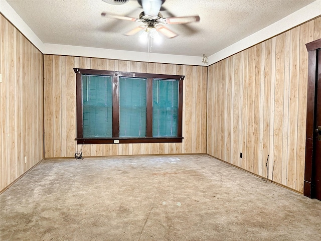 unfurnished room featuring ceiling fan, a textured ceiling, light carpet, and wood walls