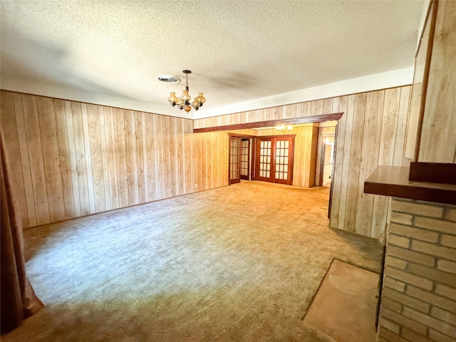 unfurnished living room featuring french doors, a textured ceiling, a notable chandelier, and wooden walls