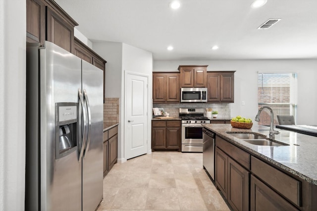 kitchen with decorative backsplash, dark brown cabinets, stainless steel appliances, sink, and stone countertops