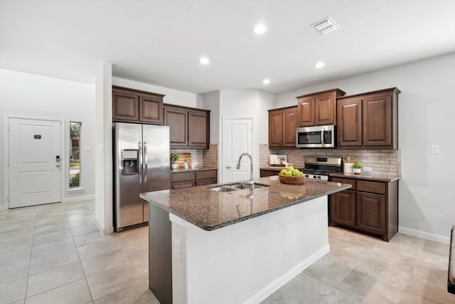 kitchen with tasteful backsplash, dark stone counters, stainless steel appliances, sink, and a center island with sink