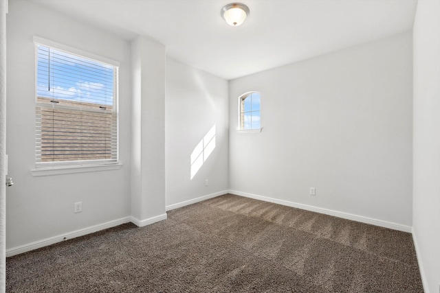 empty room featuring dark colored carpet and a wealth of natural light