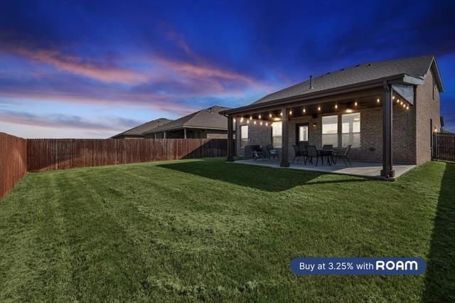 back house at dusk featuring a patio area and a yard