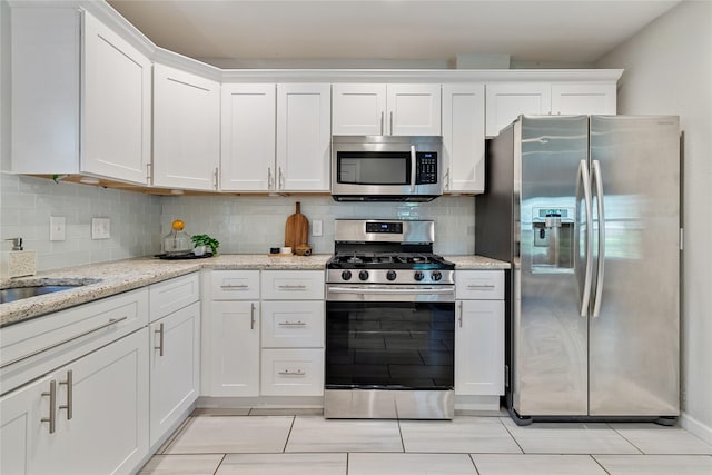 kitchen with appliances with stainless steel finishes, decorative backsplash, white cabinets, and light stone counters