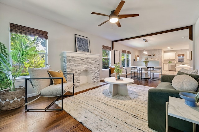 living room featuring ceiling fan, a healthy amount of sunlight, hardwood / wood-style flooring, and a stone fireplace