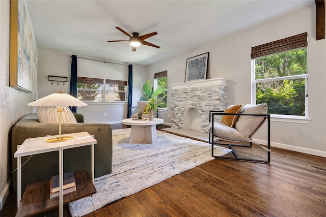 living area with ceiling fan, plenty of natural light, hardwood / wood-style floors, and a stone fireplace