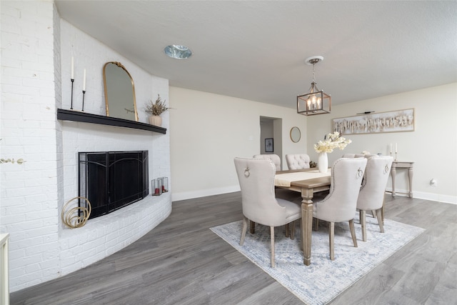 dining area with a textured ceiling, hardwood / wood-style floors, a notable chandelier, and a brick fireplace