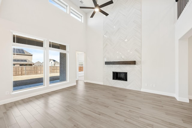 unfurnished living room with a premium fireplace, a towering ceiling, ceiling fan, and light hardwood / wood-style flooring