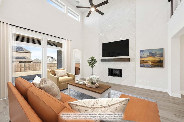 living room with ceiling fan, a high end fireplace, light hardwood / wood-style floors, and a towering ceiling