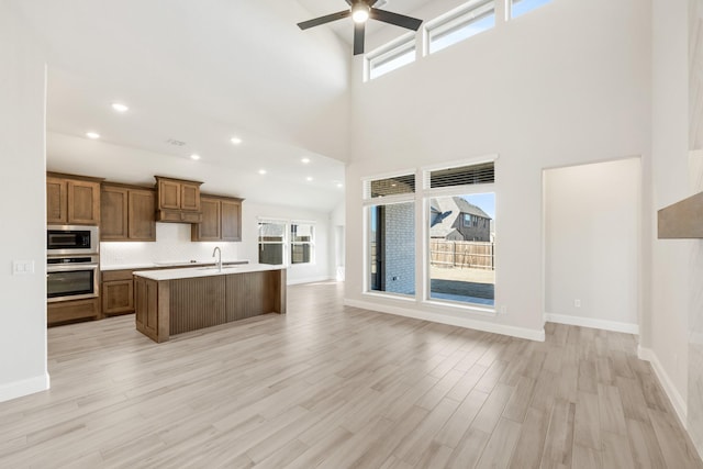 kitchen with light hardwood / wood-style flooring, a kitchen island with sink, a wealth of natural light, built in microwave, and oven