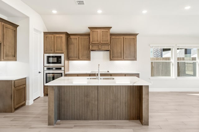 kitchen featuring sink, black microwave, light stone countertops, a center island with sink, and oven