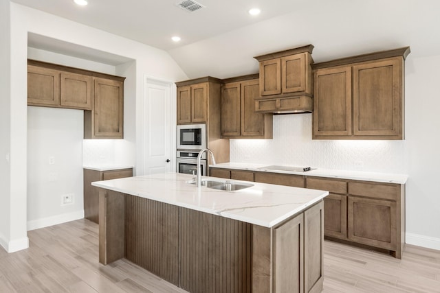 kitchen with built in microwave, sink, an island with sink, black electric stovetop, and oven