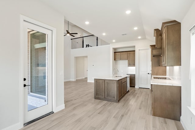 kitchen featuring lofted ceiling, sink, light hardwood / wood-style flooring, a kitchen island with sink, and black electric stovetop