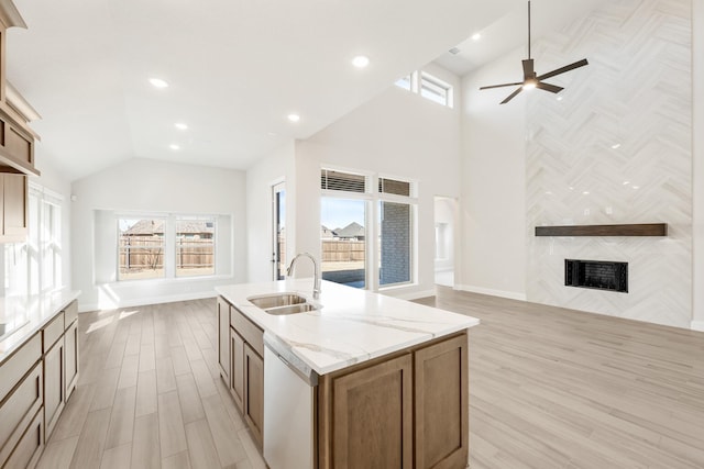 kitchen featuring sink, dishwasher, a kitchen island with sink, light stone counters, and a fireplace