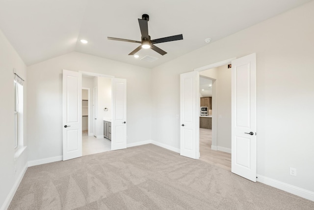 unfurnished bedroom with ceiling fan, ensuite bathroom, vaulted ceiling, and light carpet