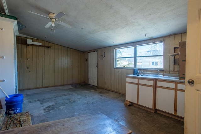 empty room with vaulted ceiling, ceiling fan, a textured ceiling, and wood walls