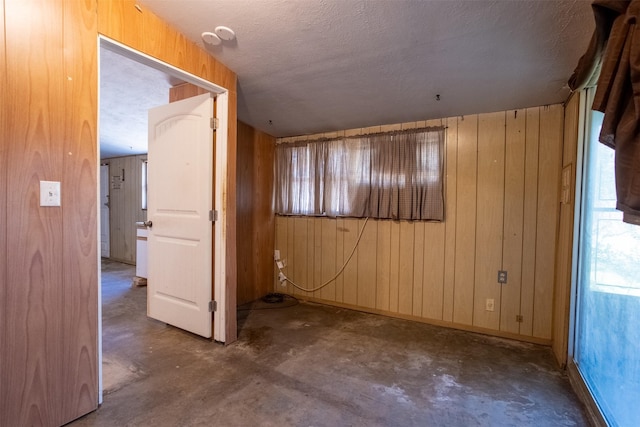 unfurnished room featuring concrete floors, a textured ceiling, and wood walls