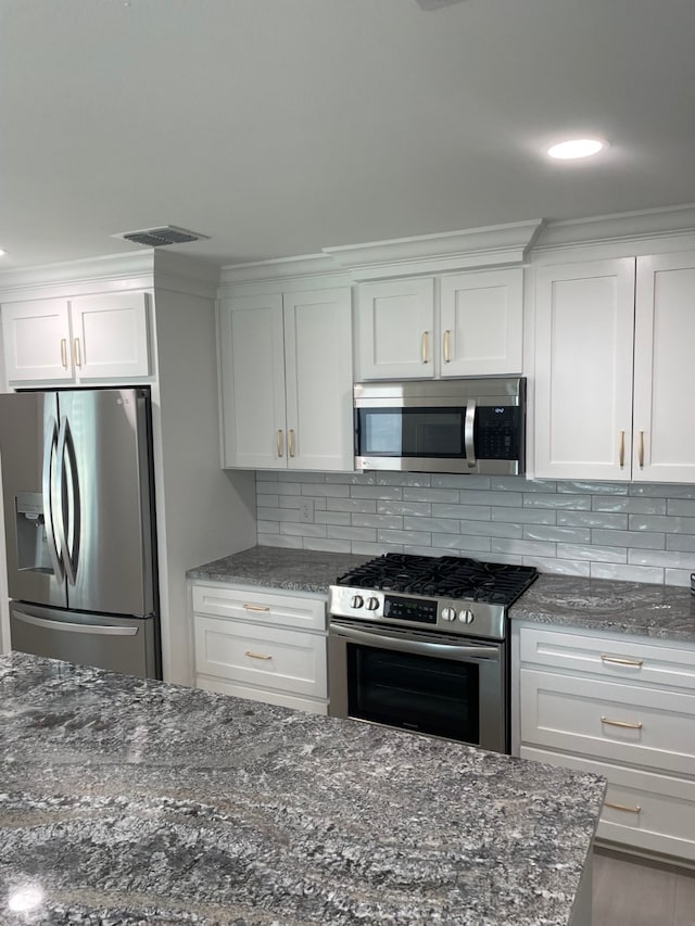 kitchen featuring stainless steel appliances, white cabinetry, dark stone countertops, and decorative backsplash