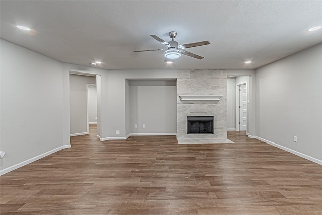 unfurnished living room with ceiling fan, a tile fireplace, a textured ceiling, and hardwood / wood-style floors