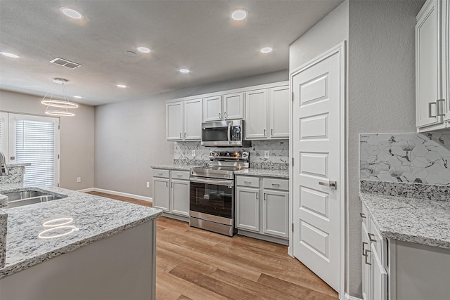 kitchen with sink, hanging light fixtures, stainless steel appliances, and tasteful backsplash