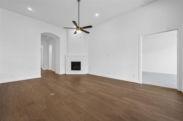 unfurnished living room with ceiling fan, a fireplace, and dark wood-type flooring