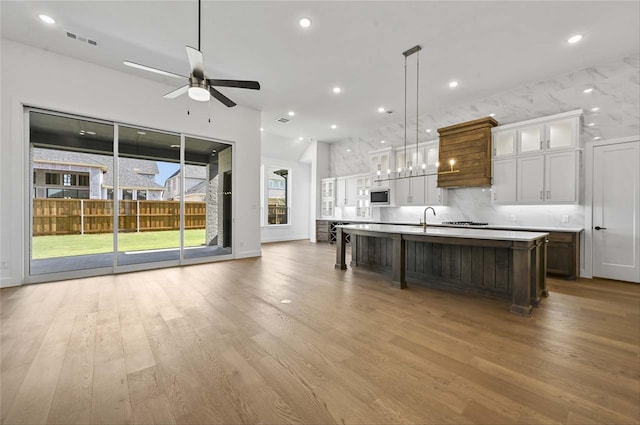 kitchen with a large island, light hardwood / wood-style floors, white cabinets, decorative light fixtures, and ceiling fan