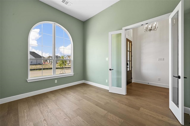 empty room with an inviting chandelier, wood-type flooring, and french doors