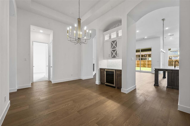 unfurnished living room featuring an inviting chandelier, beverage cooler, dark hardwood / wood-style floors, and sink