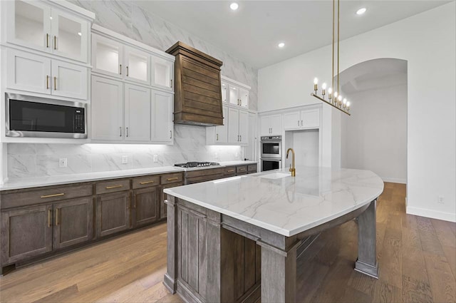 kitchen featuring appliances with stainless steel finishes, hanging light fixtures, light stone counters, hardwood / wood-style flooring, and a kitchen island with sink